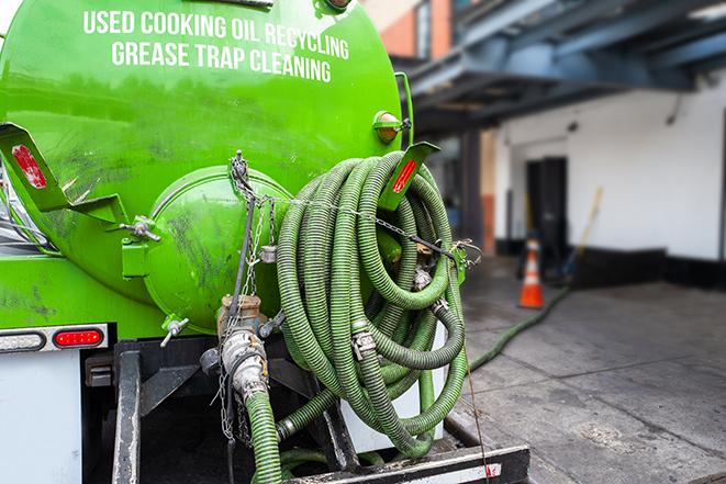 a professional plumber using a pump to empty a grease trap in Beverly